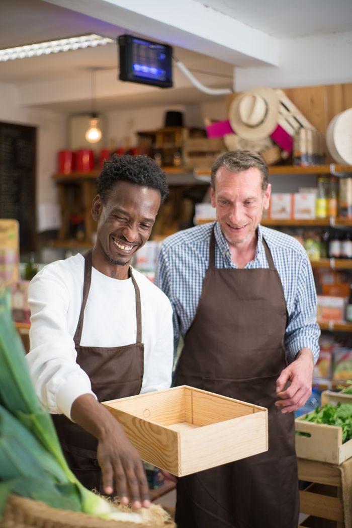 The Art of Drawing Readers In: Your attractive post title goes here Two smiling store sellers in aprons interact joyfully in a grocery store setting.